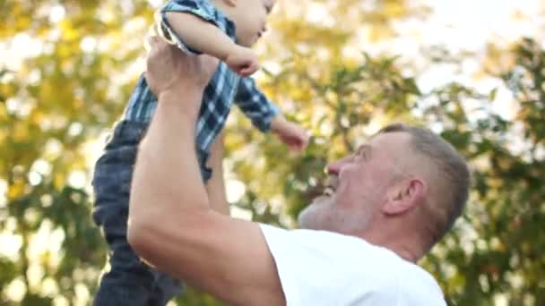 Feliz abuelo levanta a su nieto y lo besa en el estómago. Abuelo y nieto. Retrato exterior — Vídeo de stock