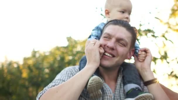 ハンサムな若い男は彼の小さな息子の肩に保持します。村の夏休み。同時代の三人の男の肖像 — ストック動画