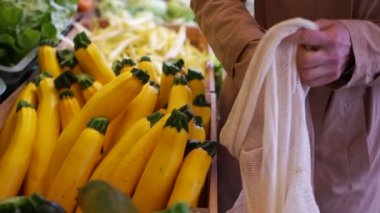 Kadınlar süpermarkette kabak seçiyor. Bir kadın sarı kabağı ekolojik ambalajda katlıyor, bir kumaş torbasında. Plastiği durdur