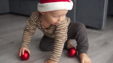 Noel Baba postu şapkalı çocuk kırmızı bir Noel topuyla oynuyor. Mutlu Noeller ve mutlu yıllar.