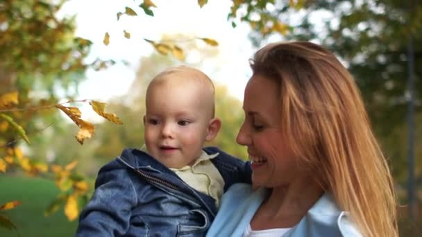 Madre che abbraccia suo figlio durante una passeggiata nel parco. Madre e figlio strappano foglie gialle da un albero. Festa della mamma, passeggiata autunnale con il bambino — Video Stock