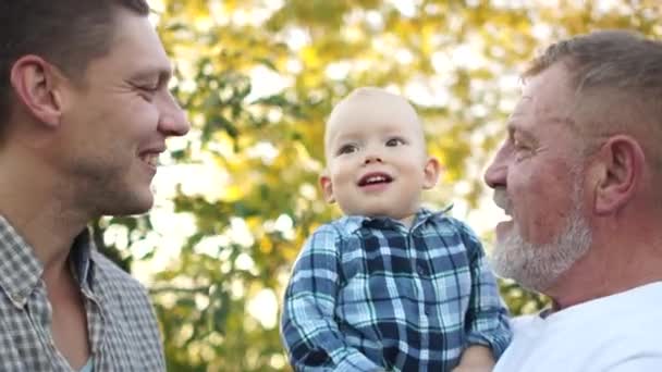 Egy kisgyerek az apjával és a nagyapjával a nyári kertben. Szoros zsákmány, boldog család — Stock videók
