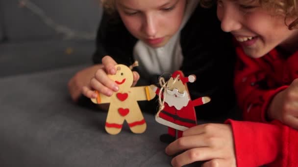 Niño y niña, los mejores amigos vestidos con pijamas de Navidad, se divierten jugando con figuras de madera para decorar el árbol de Navidad. Nochebuena — Vídeos de Stock