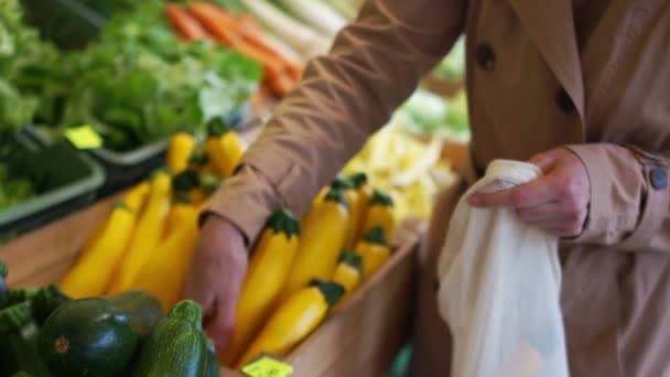 Frauenhände pflücken auf dem Markt gelbe Zucchini vom Tablett. Mehrwegverpackungen, gewebte Beutel — Stockvideo