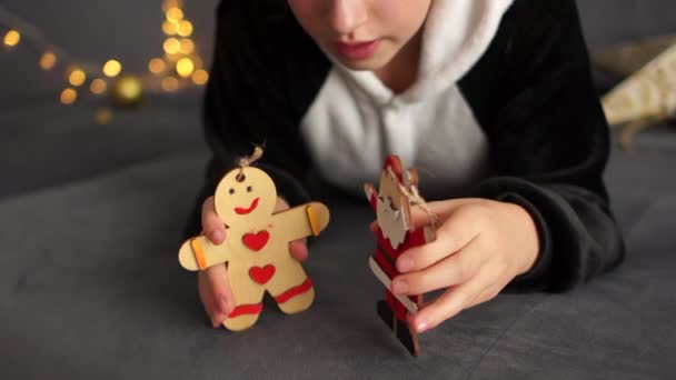 Η σγουρή μαθήτρια με τις πιτζάμες παίζει με ξύλινες χριστουγεννιάτικες φιγούρες. Προετοιμασία για το Χριστουγεννιάτικο πάρτι, Πρωτοχρονιάτικες διακοπές — Αρχείο Βίντεο