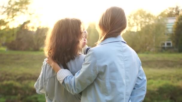 Couple homosexuel avec un bébé dans les bras pour une promenade dans le parc d'automne. Deux femmes se tiennent debout embrassant et regardant le coucher du soleil, vue arrière — Video