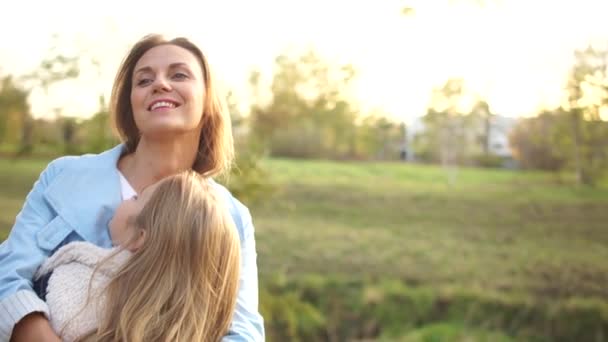 Boldog család, anya és lánya ölelkeznek a városi őszi parkban a lenyugvó nap ellen. A lányok vidáman mosolyognak — Stock videók