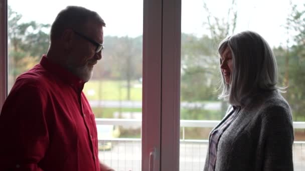 Mature couple wishes each other a Merry Christmas. A man gives a woman a Christmas present in a beautiful package. Close portrait on against the window — Stock Video