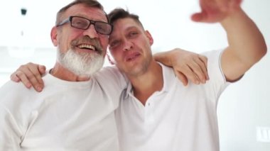 Mutlu iki nesil. Yaşlı baba gülüyor. Küçük oğlu kucaklıyor, büyük baba yetişkin adama sarılıyor. Babalar günü, yaş farkı.