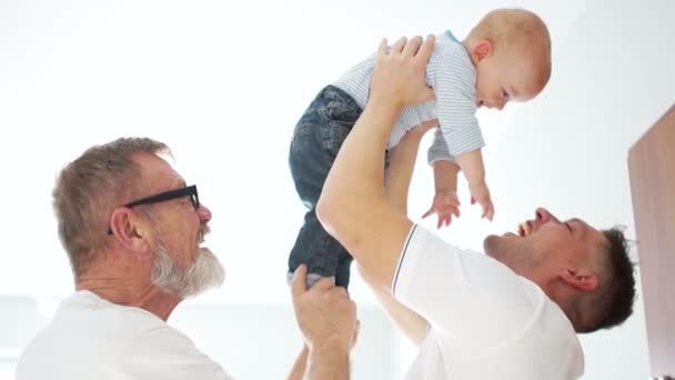 Tre generazioni di una sola famiglia. Tre uomini, nonno, padre e nipote. Festa dei padri. Gli uomini abbracciano il bambino indore nella stanza bianca — Video Stock