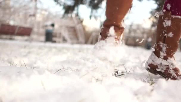 Close-up de botas castanhas femininas na neve. Uma criança joga bolas de neve e pula na neve — Vídeo de Stock