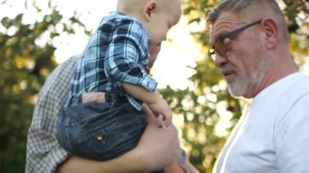 Avô feliz e neto estão brincando no jardim de outono durante a colheita. Família encantadora, três gerações de homens da mesma família, retrato próximo, brilho solar — Vídeo de Stock