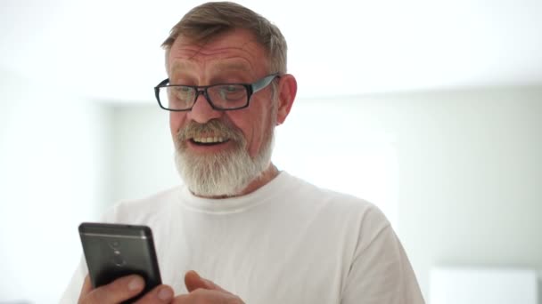 Retrato de perto de um homem bonito com um telemóvel nas mãos. Avô recebeu uma mensagem de seu neto, um aposentado moderno — Vídeo de Stock