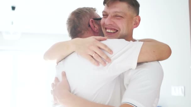 Homens atraentes abraço, diferença de idade, pai e filho, em um fundo branco em roupas brancas, dia dos pais — Vídeo de Stock