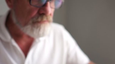 Dizüstü bilgisayarla çalışırken gözlüklü, gri, olgun bir adam. Mutlu yaşlılar, aktif emekliler, iş konsepti
