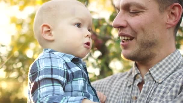 Feliz jovem pai abraça seu filho de dois anos de idade no parque de outono. Homem rindo alegremente, dia dos pais, retrato próximo — Vídeo de Stock