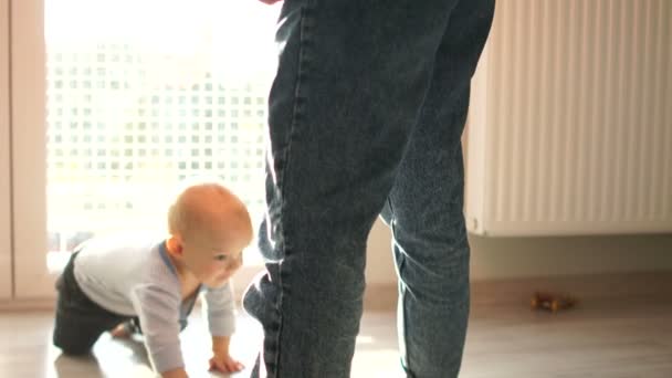 Toddler és anya jól érzik magukat otthon. Egy baba mászik a földön, és kúszik az anyák lába között. — Stock videók