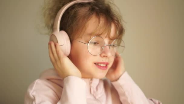 Portrait of a teenage girl with headphones on her head, wearing glasses. Girl listens to music on headphones and dances, youth hobby, melomania — Stok video