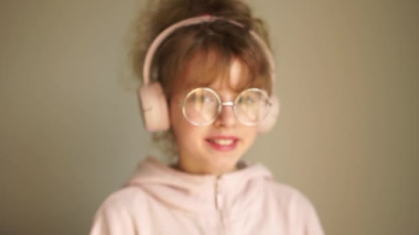 Chica escucha música en los auriculares y bailes, afición juvenil, melomanía. Retrato de una adolescente con auriculares en la cabeza, con gafas — Vídeo de stock