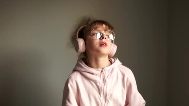 Милая девушка-подросток в очках и с вьющимися волосами слушает музыку с помощью беспроводных наушников. Технология Bluetooth, современный плейлист — стоковое видео