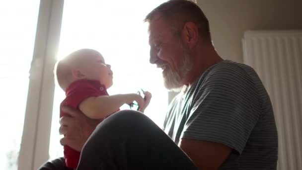 Close indoors portrait grandfather plays with his 18 month old grandson. Sun glare, good grandfather, grandfather and grandson, happy family — ストック動画