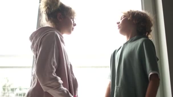 Boy and a girl are standing against each other Indoor in front of the window. Children bully to each other, quarrel, bullying at school — Stockvideo