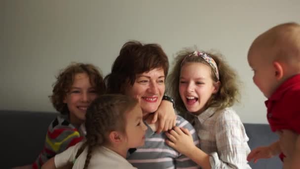 Loving good grandmother and her four grandchildren are hugging while sitting on the couch. Woman babysitter with her children — Stockvideo