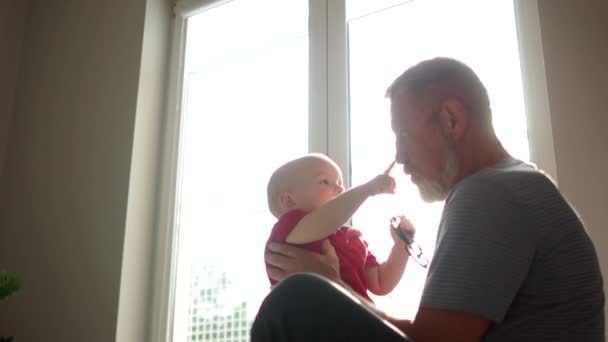 Il nonno sta giocando col suo nipotino. Un bambino con una maglietta rossa si diverte sul pavimento con un nonno dalla barba grigia — Video Stock