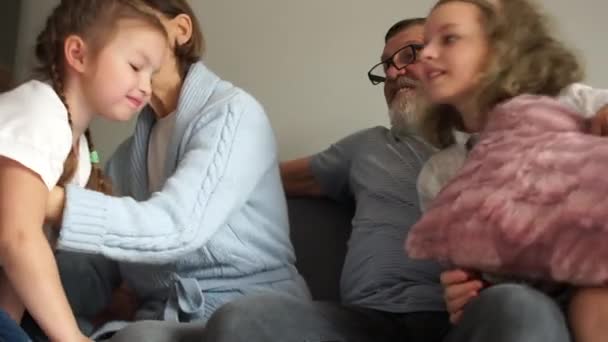 Большая семья из пяти человек обнимается, сидя на диване. Дедушка и бабушка с тремя внуками, счастливая семья, зимние каникулы — стоковое видео