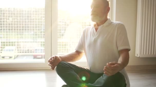 Yoga lessen. Spirituele oefening, een oudere yogi zit op de vloer in een lotuspositie. Zonneschijn — Stockvideo