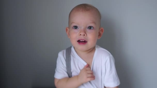 Portret van de jongen met de blauwe ogen in een wit T-shirt. De jongen is beschaamd, kinderen emoties, gelukkige jeugd, aanpassing van het kind in de kleuterschool — Stockvideo