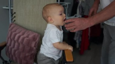 Adam çocuğa bir bardak temiz su tutuyor. İçme modu. İki yaşındaki bir bebek bardaktan su içiyor, bir evin portresi.