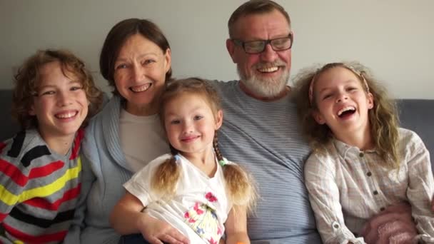 Los nietos y sus abuelos están sentados abrazados en el sofá. Familia feliz, abuelos y tres nietos — Vídeos de Stock