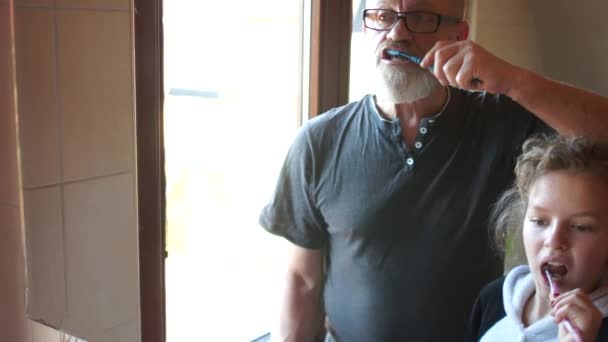 Grandfather and granddaughter brush their teeth before zarkal in the bathroom. Good example, morning dental hygiene, happy family — ストック動画