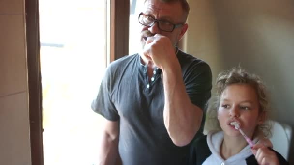 Morning dental hygiene. Grandfather and granddaughter brush their teeth before zarkal in the bathroom. Good example, happy family — ストック動画