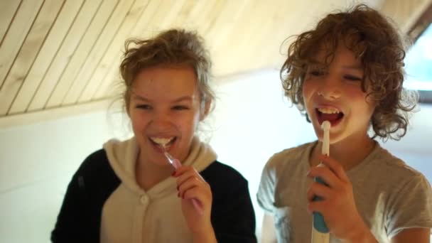 Çocuk elektrikli diş fırçası kullanıyor. Erkek ve kız kardeş dişlerini aynanın karşısındaki banyoda fırçalıyorlar. Diş hijyeni, çocuklar dişlerini fırçalar. — Stok video