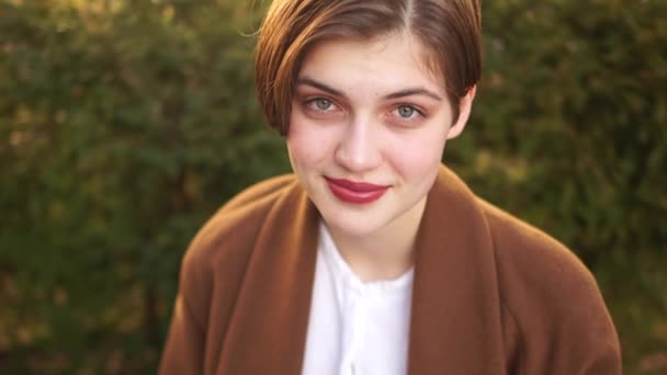 Retrato de perto de uma bela jovem com um corte de cabelo curto e um sorriso de dentes brancos. Mulher feliz, retrato ao ar livre — Vídeo de Stock