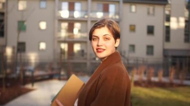 Gün batımında büyük bir apartmanın arka planında çekici genç bir kadın. Yakın portre, iş kadını, mutlu kadın.