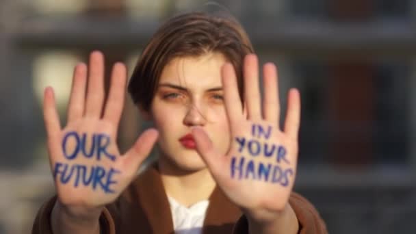 Junge Frau protestiert gegen die globale Erwärmung. Klimaschlag, Umweltkatastrophe. Nahaufnahme einer schönen Studentin mit einer Inschrift auf den Handflächen. unsere Zukunft in Ihren Händen — Stockvideo