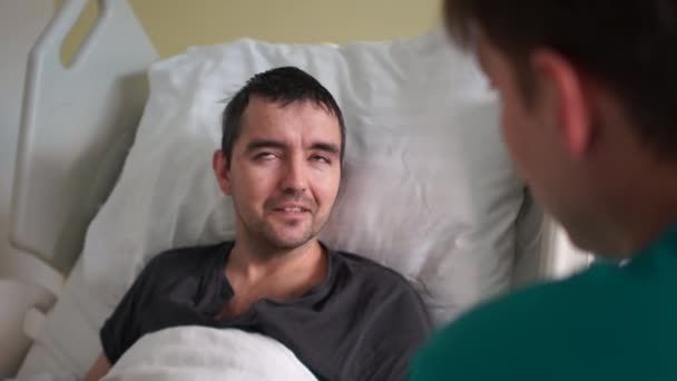 Återhämtning efter en stroke. En ung man ligger i sängen bredvid en läkare eller sjuksköterska. Sjukhusbehandling — Stockvideo
