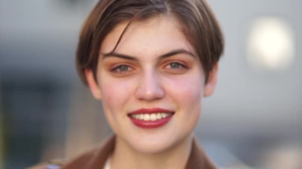 Close outdoor portrait of a beautiful smiling girl with a short haircut and red lipstick on her lips. Happy woman — Stock Video