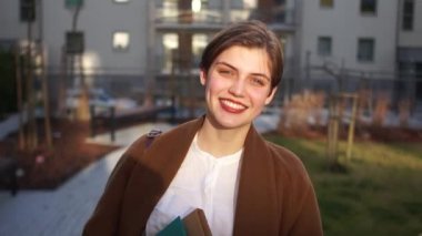 Portrait of a smiling young realtor woman in the courtyard of a new city building. Happy woman, real estate, housewarming