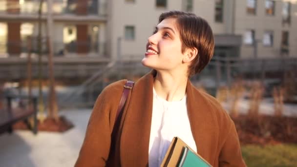 Beautiful student goes to university, holds textbooks and abstracts in rukaz. Sunset, city portrait — Stok video