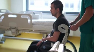 Özürlü genç adam hastanede tekerlekli sandalyeden kalkar. Bir hemşire ona yardım ediyor. Felç sonrası iyileşme ve rehabilitasyon, araba kazası sonrası rehabilitasyon