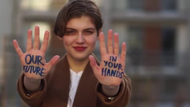 Fiatal lány, rövid hajjal, felirattal a kezén - a jövőnk a te kezedben van. Globális éghajlatváltozás. Előtte nyújtja ki a kezét. — Stock videók
