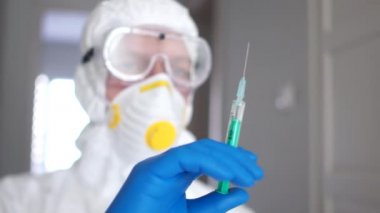 Koruyucu kıyafetli, maskeli ve solunum cihazlı bir adamın portresi koronavirüsü olan bir hasta için enjeksiyon hazırlıyor. Tıbbi araştırma, koronavirüs aşısı.