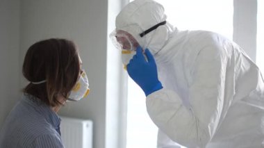 Koruyucu giysili maskeli bir adamın portresi enfekte bir kadını muayene ediyor. Coronavirüs belirtileri