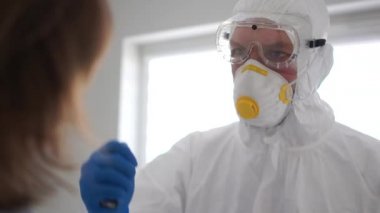 Koruyucu giysili bir doktor, şüpheli koronavirüsü olan insanları muayene ediyor. Ağzına bir el feneri tutar. Koronavirüs salgını, sınır izolasyon koğuşu, salgın önleme