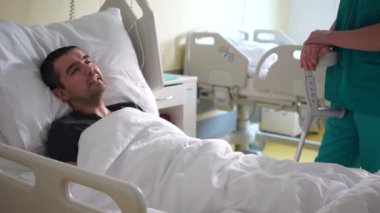 Özürlü genç bir adam yatakta uzanıp doktoruyla konuşuyor. Felç sonrası iyileşme, ağır hasta bir adam.