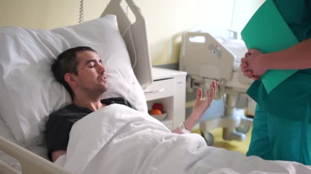 Zotavení z mrtvice, vážně nemocný muž. Mladý muž se zdravotním postižením leží v posteli a mluví se svým doktorem — Stock video